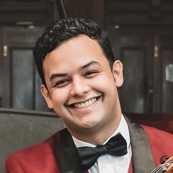 A man with short curly hair wearing a red jacket, white shirt, and black bow tie smiles at the camera.